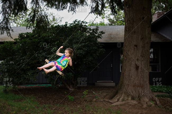 Girl Wearing Tie Dyed Dress Swinging On A Backyard Tree Swing