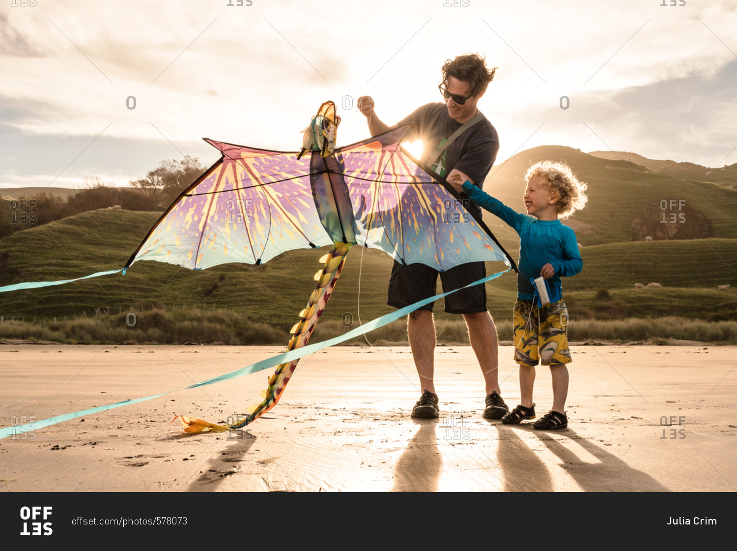 Man helping his toddler son fly dragon kite on beach