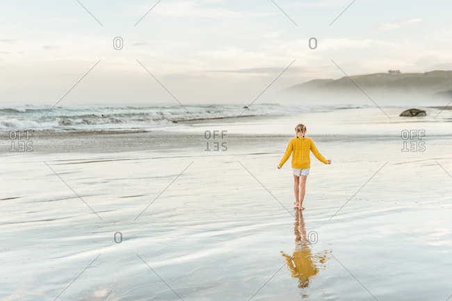 Girl in yellow sweater walking on beach