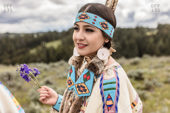 Girl holding purple flowers while wearing in Native American regalia