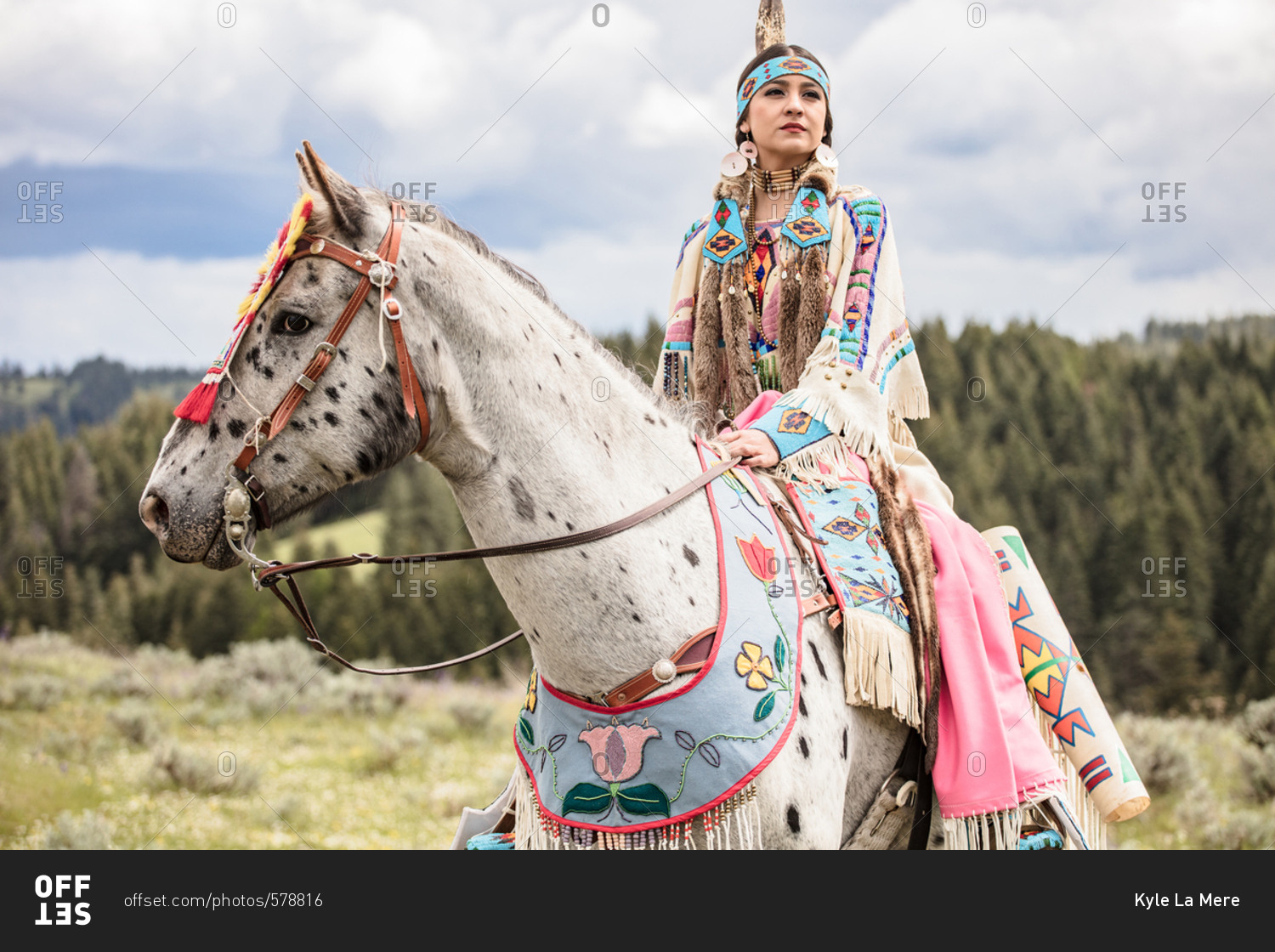 Native American young woman dressed in regalia riding a spotted horse
