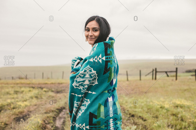 Smiling young woman wrapped in a blue woven blanket in field