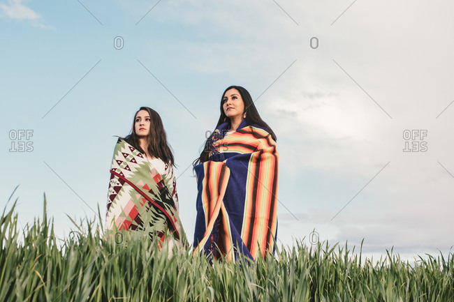 Two sisters wearing woven blankets standing in a field