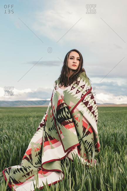 Woman wrapped in woven blanket in field