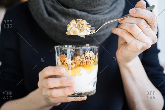 Woman holding glass and spoon with yogurt, granola and honey
