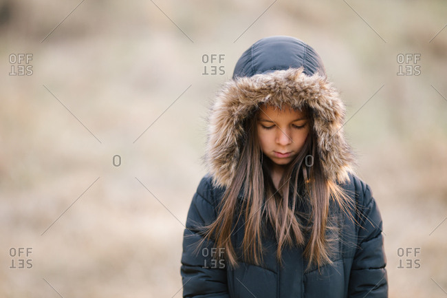 Young girl wearing winter jacket with furry hood looking down