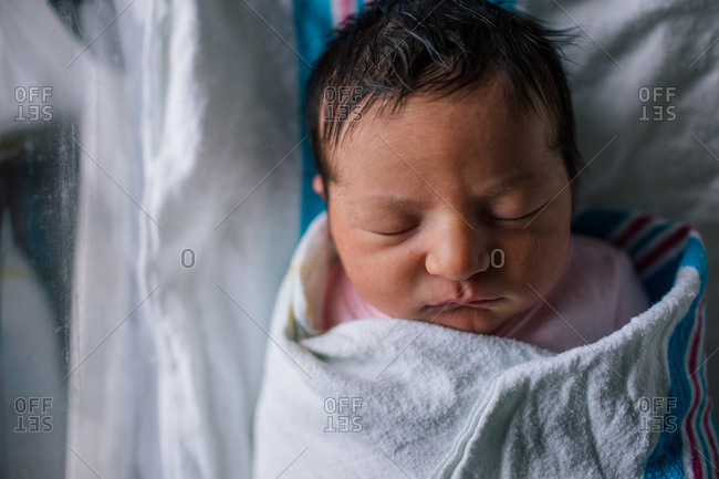 Close up of a newborn baby with thick dark hair swaddled in hospital bed  stock photo - OFFSET