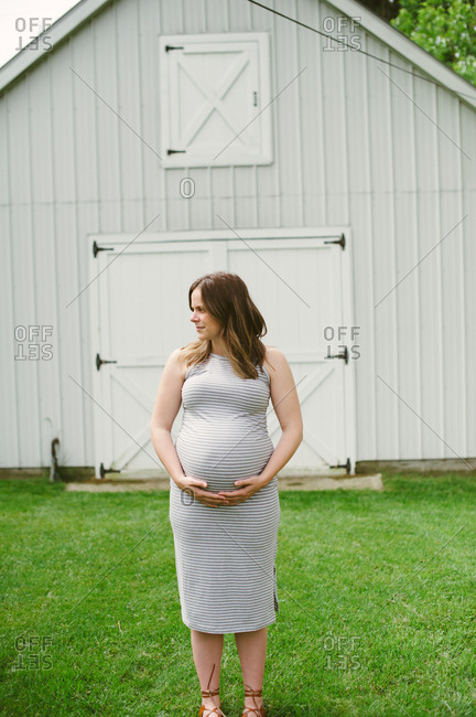Portrait of a pregnant woman in thirds trimester standing in front of barn
