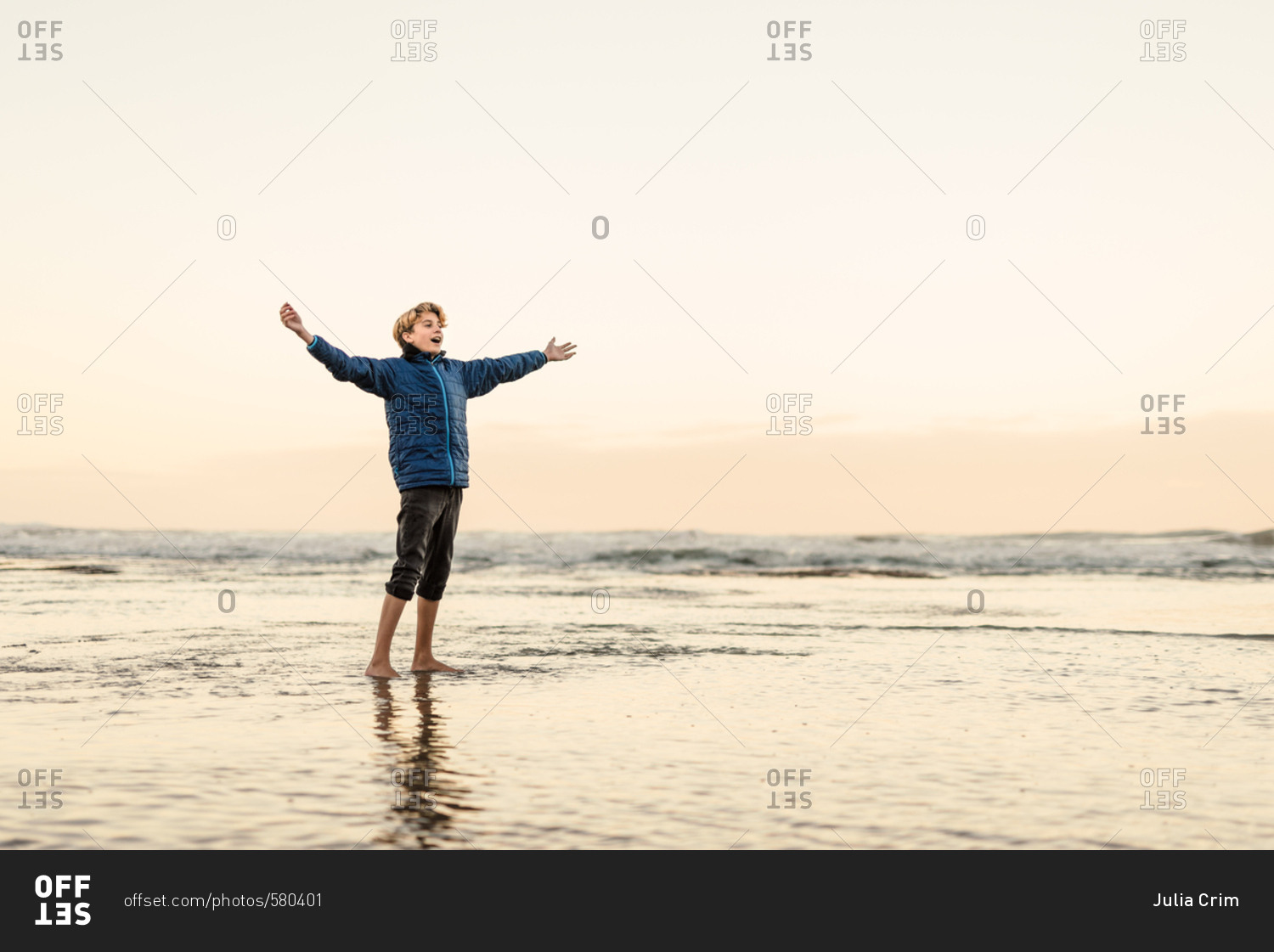 Adolescent boy standing with arms out on beach