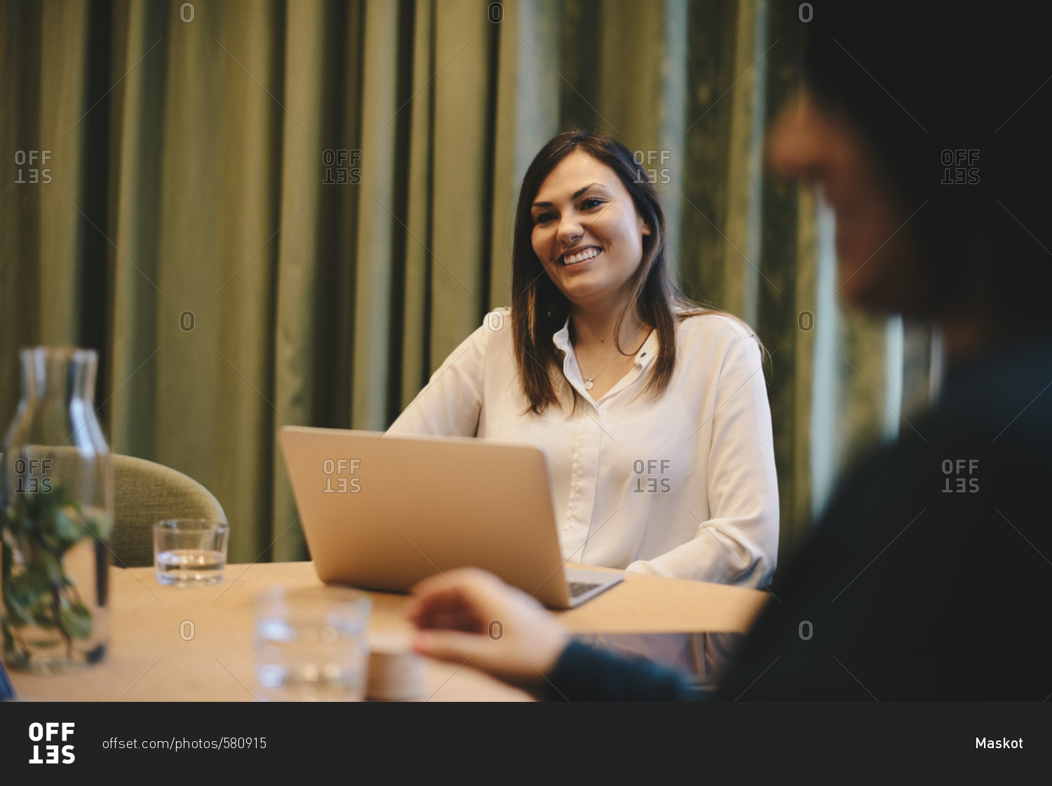 Happy businesswoman sitting wit laptop at conference table in board room