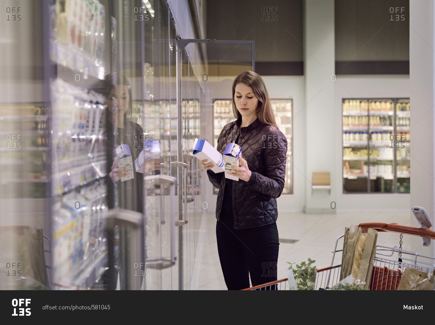 Woman holding juice boxes at refrigerated section in supermarket