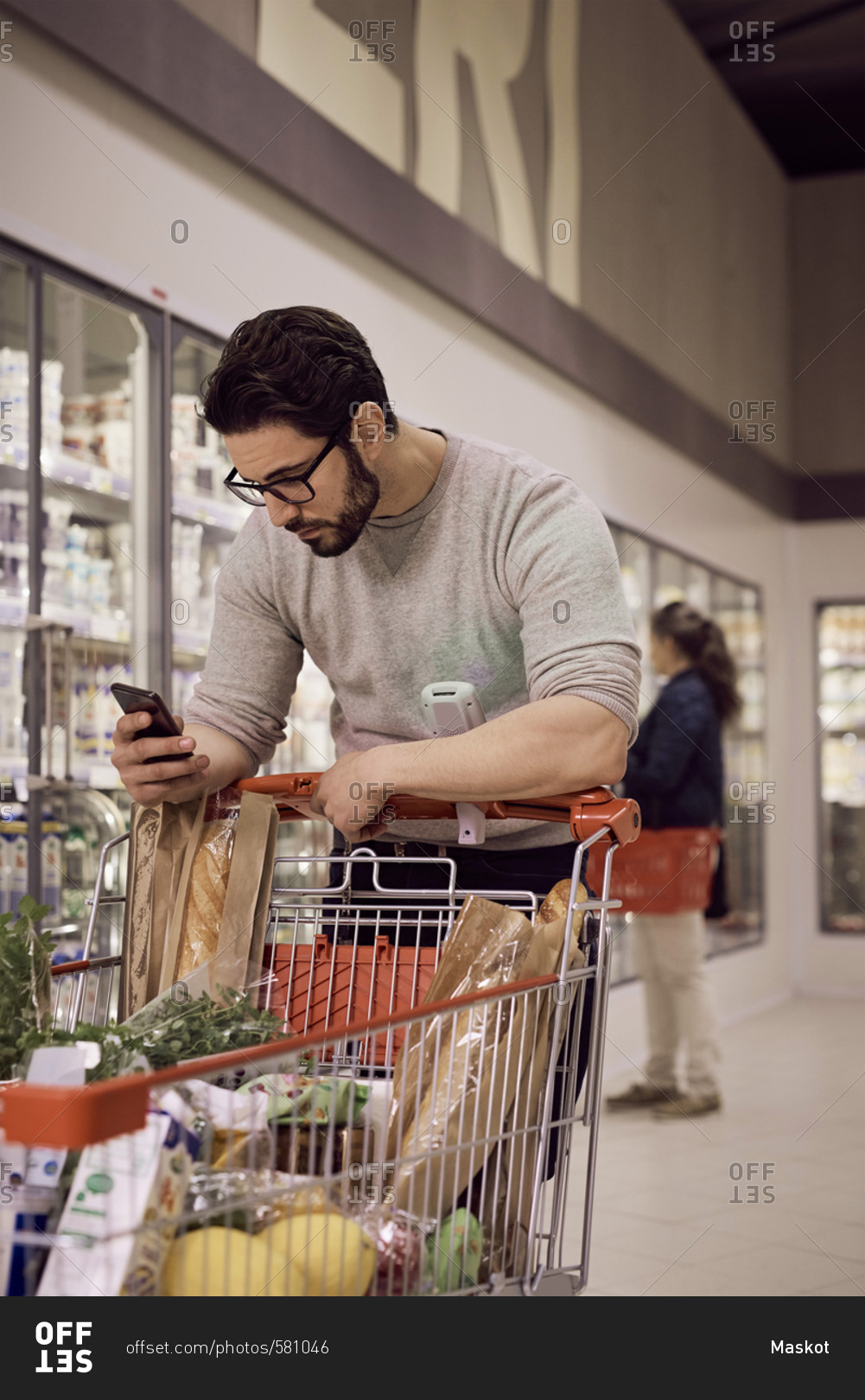 Man text messaging while leaning on shopping cart at refrigerated section in supermarket