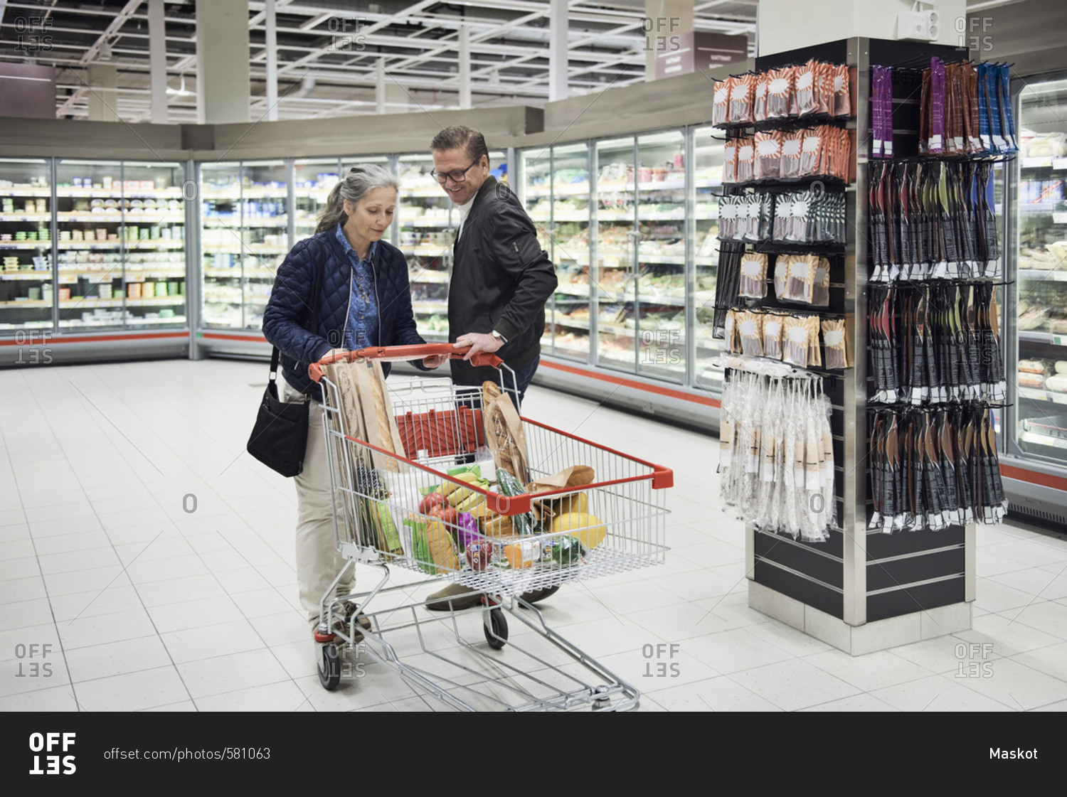 Mature couple with groceries in shopping cart at refrigerated section of supermarket