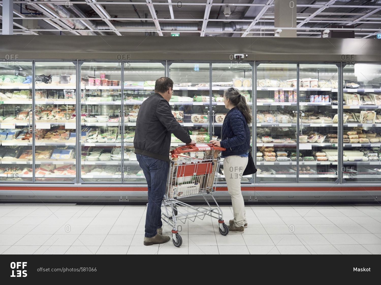 Mature couple looking at food on display at refrigerated section in supermarket