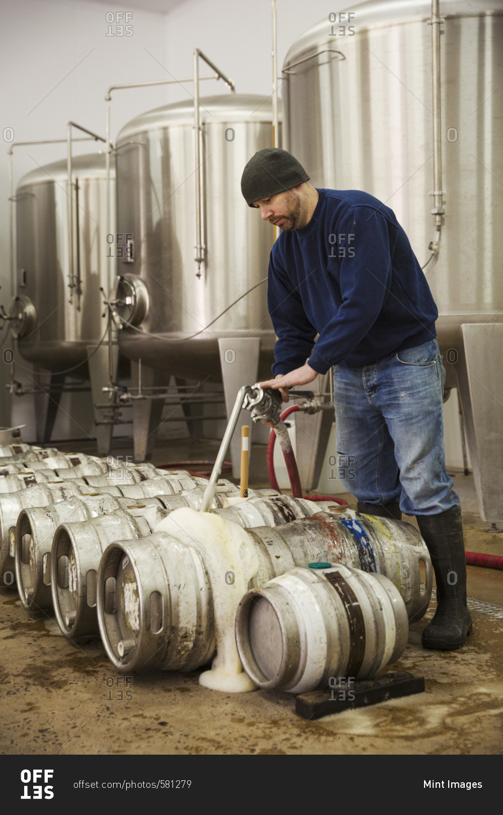 Man filling metal beer kegs with foaming beer from the fermentation chambers in a brewery