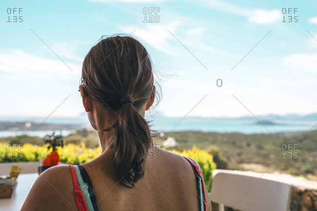 Summer vacation woman sitting at outdoor cafe with mountain view Rear view