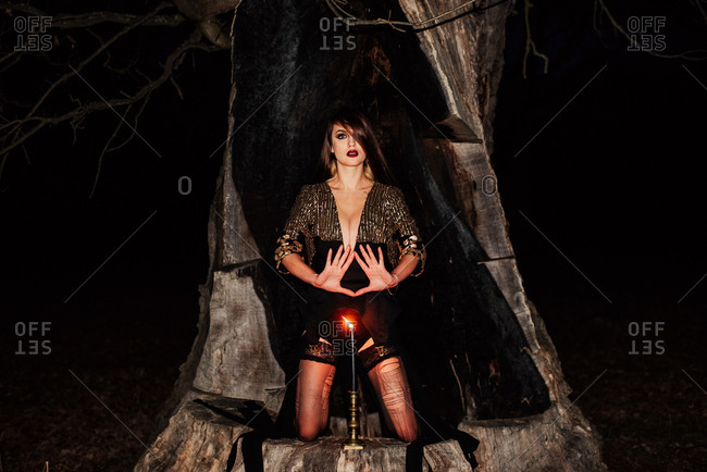 Woman in a black dress making a hand gesture behind a lighted candle on a tree stump