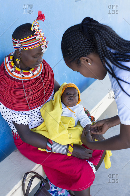 Nurse examining a infant on a mother's lap in Kenya, Africa