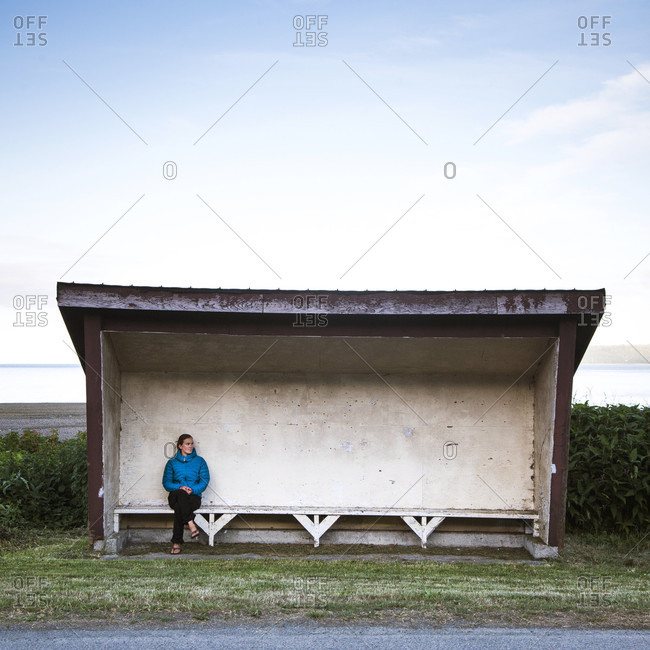 A woman sits alone in a covered buss top with water in the distance