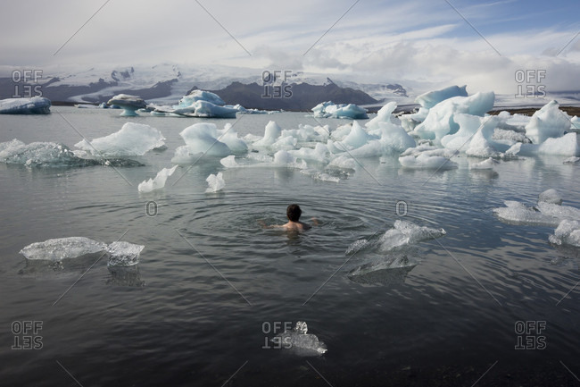 Man bathing naked in a glacier lagoon surrounded by icebergs and looking into the distance