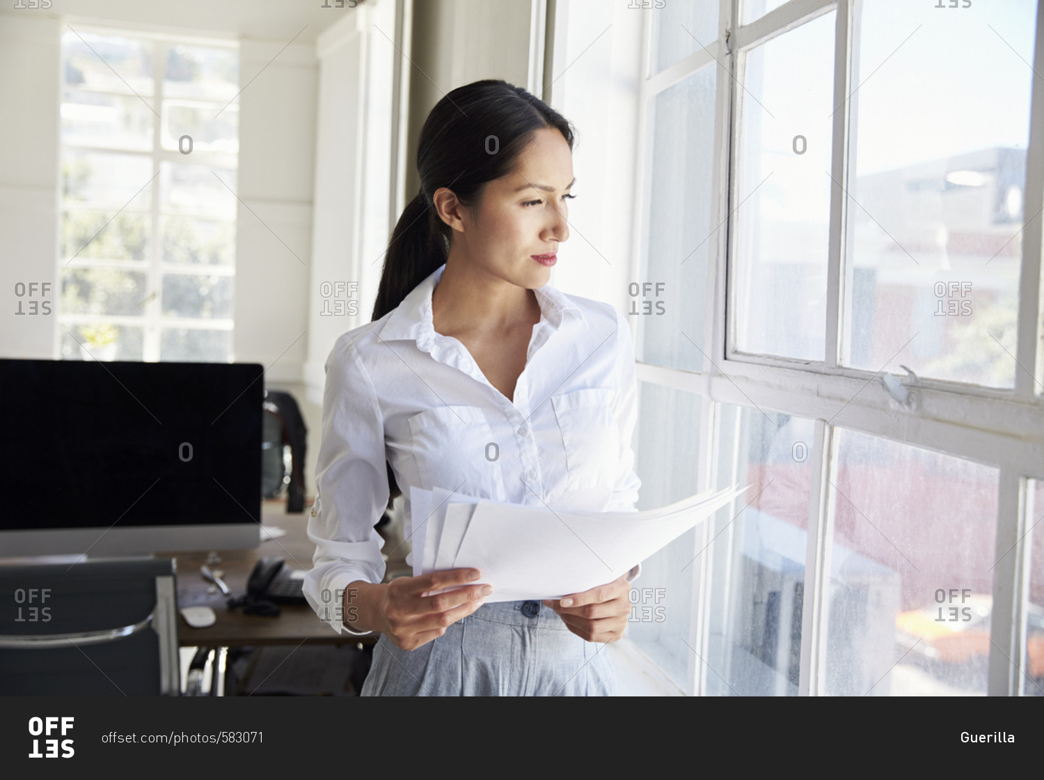 Young businesswoman holding papers looking out of window