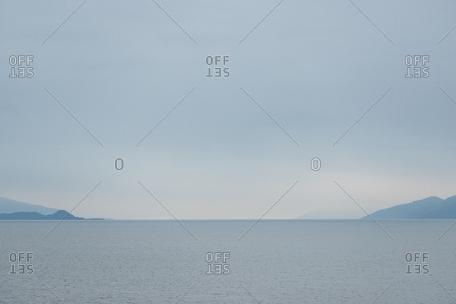 Silhouettes of mountains frame the calm horizon of ocean water under blue mist and fog