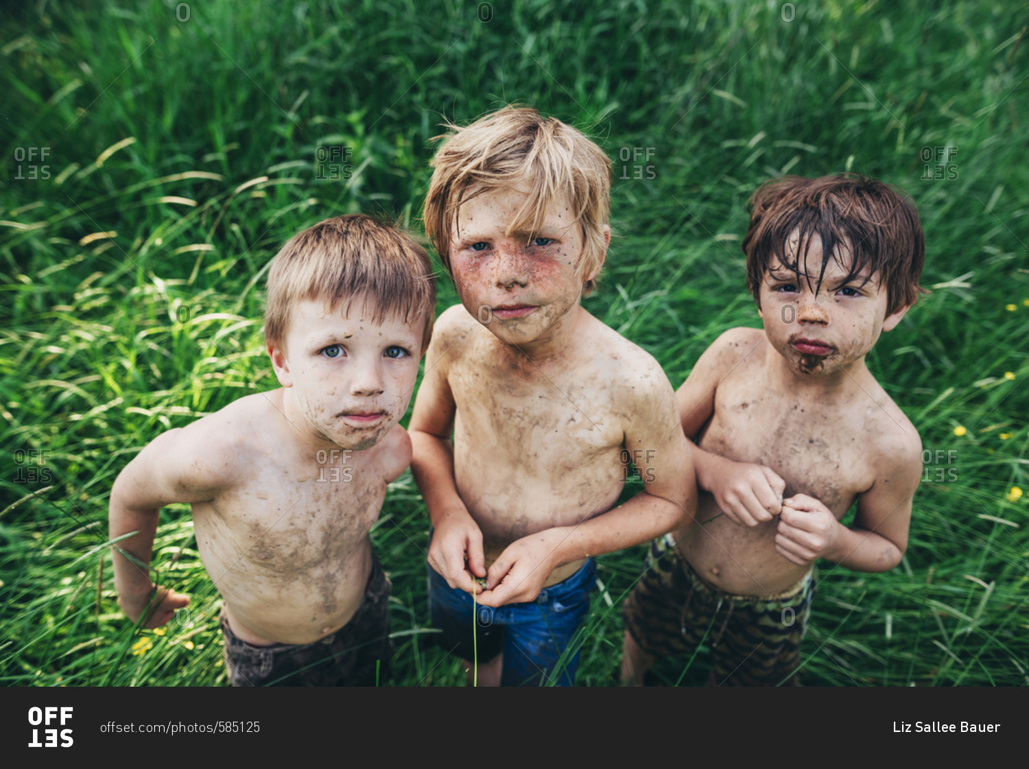 Serious young boys covered in dirt playing in tall grass in the summer