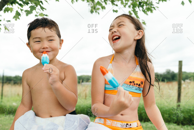 Laughing girl sitting next to brother eating red, white, and blue ice pop