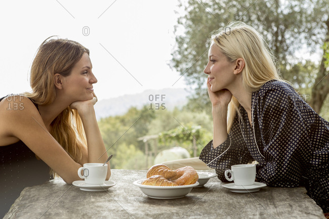 Two smiling face to face friends at breakfast table