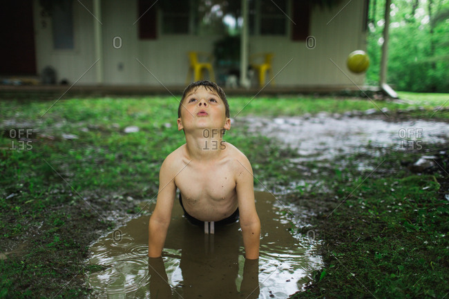 Boy playing in a backyard mud puddle