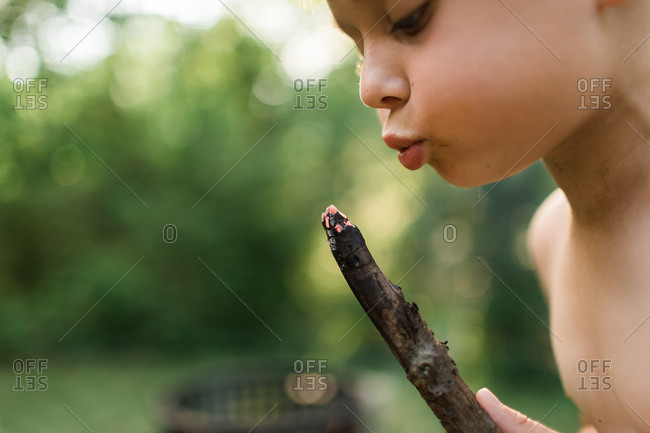 Young boy blowing on embers of burning stick