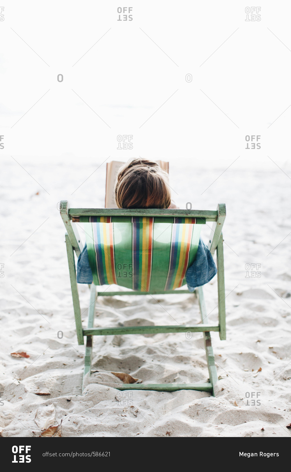 Young woman relaxes on the beach in a lounge chair while reading a book