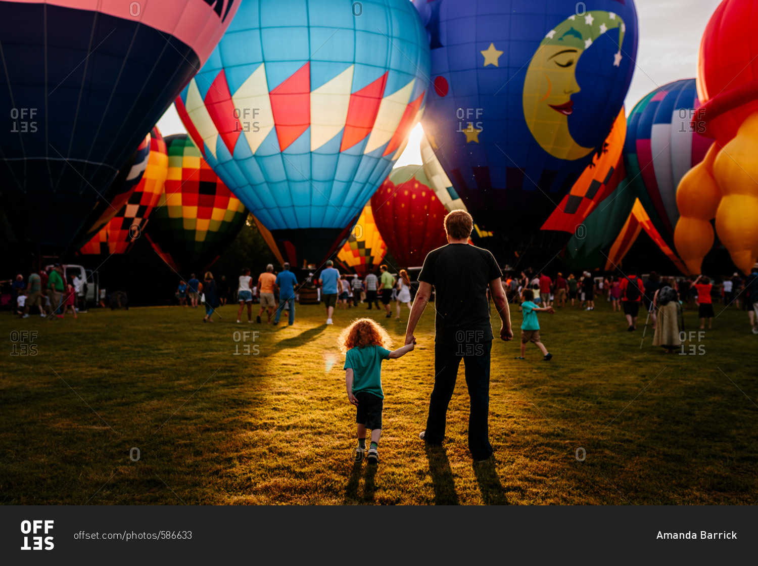 Father and son walking towards hot air balloons with crowd
