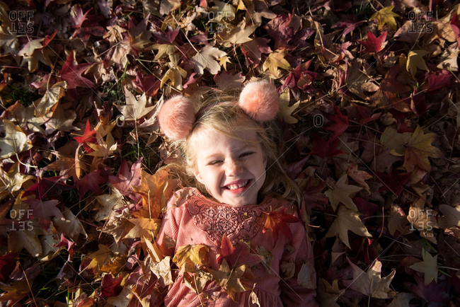 Little girl in pom-pom headband lying in leaves