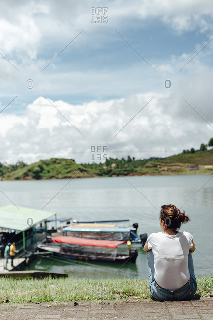 Woman having a break seated on the grass looking at Guatape lake in Guatape, Colombia