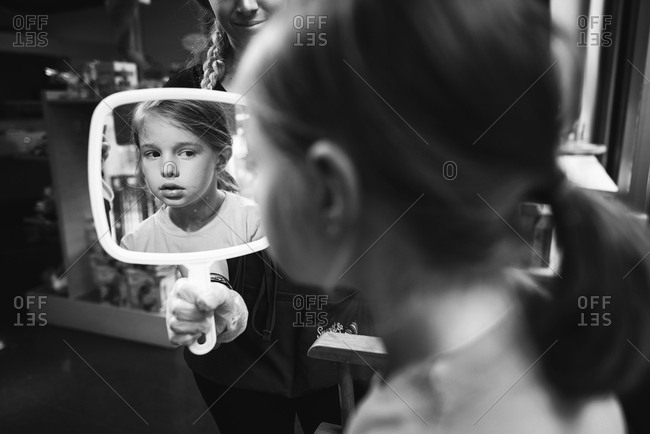 Girl looking at her pierced ears in her reflection in mirror