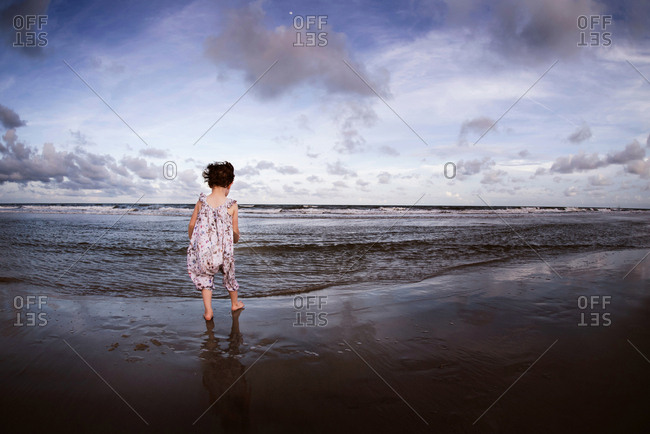 Little girl watching the waves on the beach at nightfall