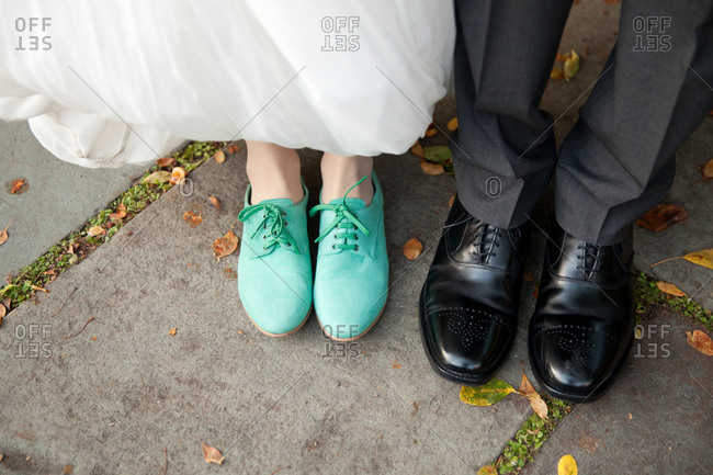 Shoes of a bride and groom standing on a sidewalk in a park
