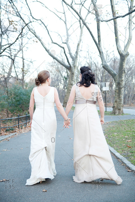 Two brides holding hands walking on a path in Central Park