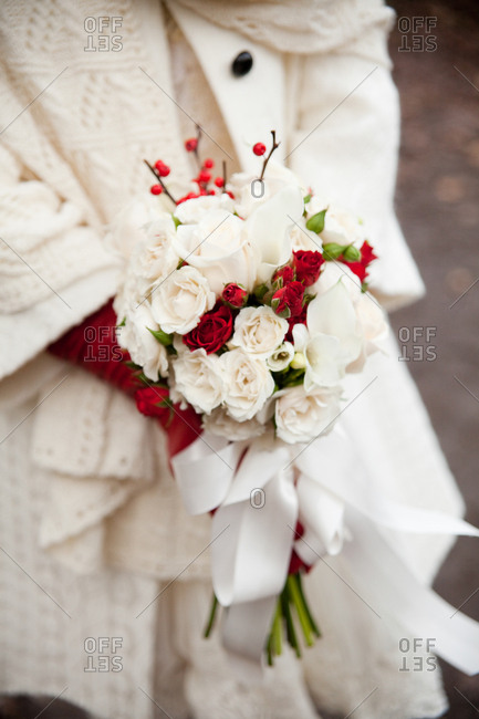 Bride wrapped in a white sweater holding a bouquet of red and white roses