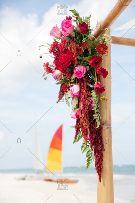 Floral arrangement with red and pink roses hanging from a wooden frame on a beach