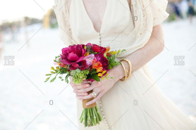 Bride on a beach holding a bouquet of pink, orange and green flowers