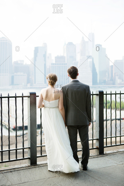 Bride and groom standing at a railing looking at a city skyline