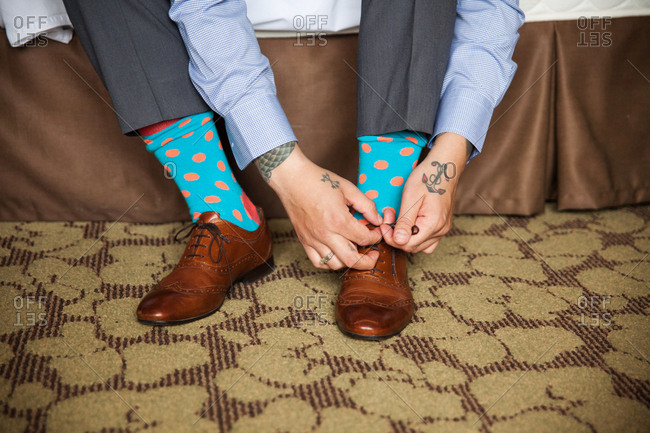 Hands of a man with polka dot socks tying brown leather loafers