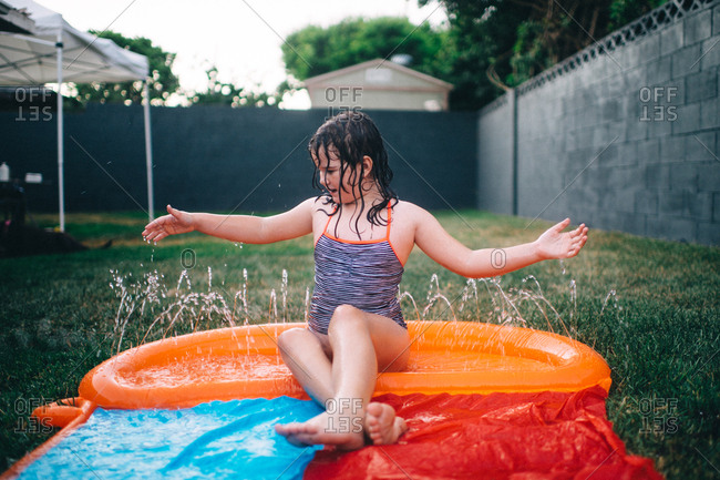 Young girl sitting in pool of water on backyard water slide