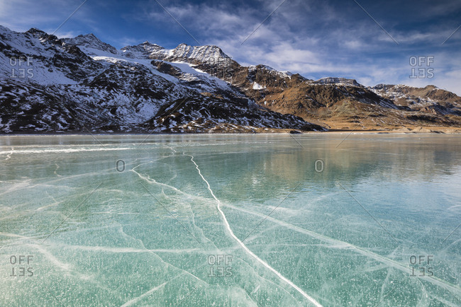 The snowy peaks frame the frozen turquoise water of White Lake (Lago Bianco), Bernina Pass, Canton of Graubunden, Engadine, Switzerland, Europe