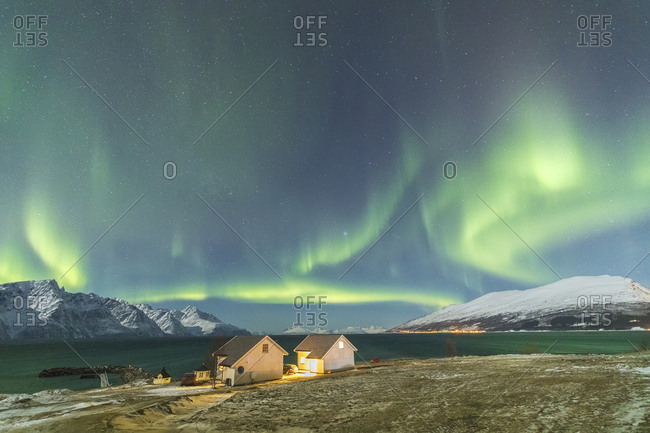 The Northern Lights (aurora borealis) and stars illuminate the wood houses called Rorbu by the sea, Djupvik, Lyngen Alps, Troms, Norway, Scandinavia, Europe
