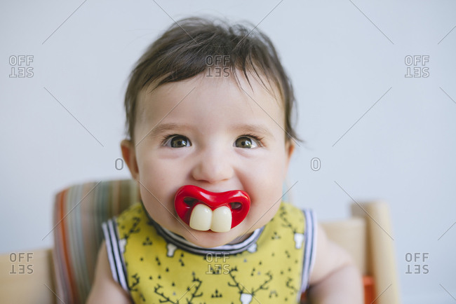 Portrait of baby girl sucking a pacifier with false teeth and mouth stock  photo - OFFSET