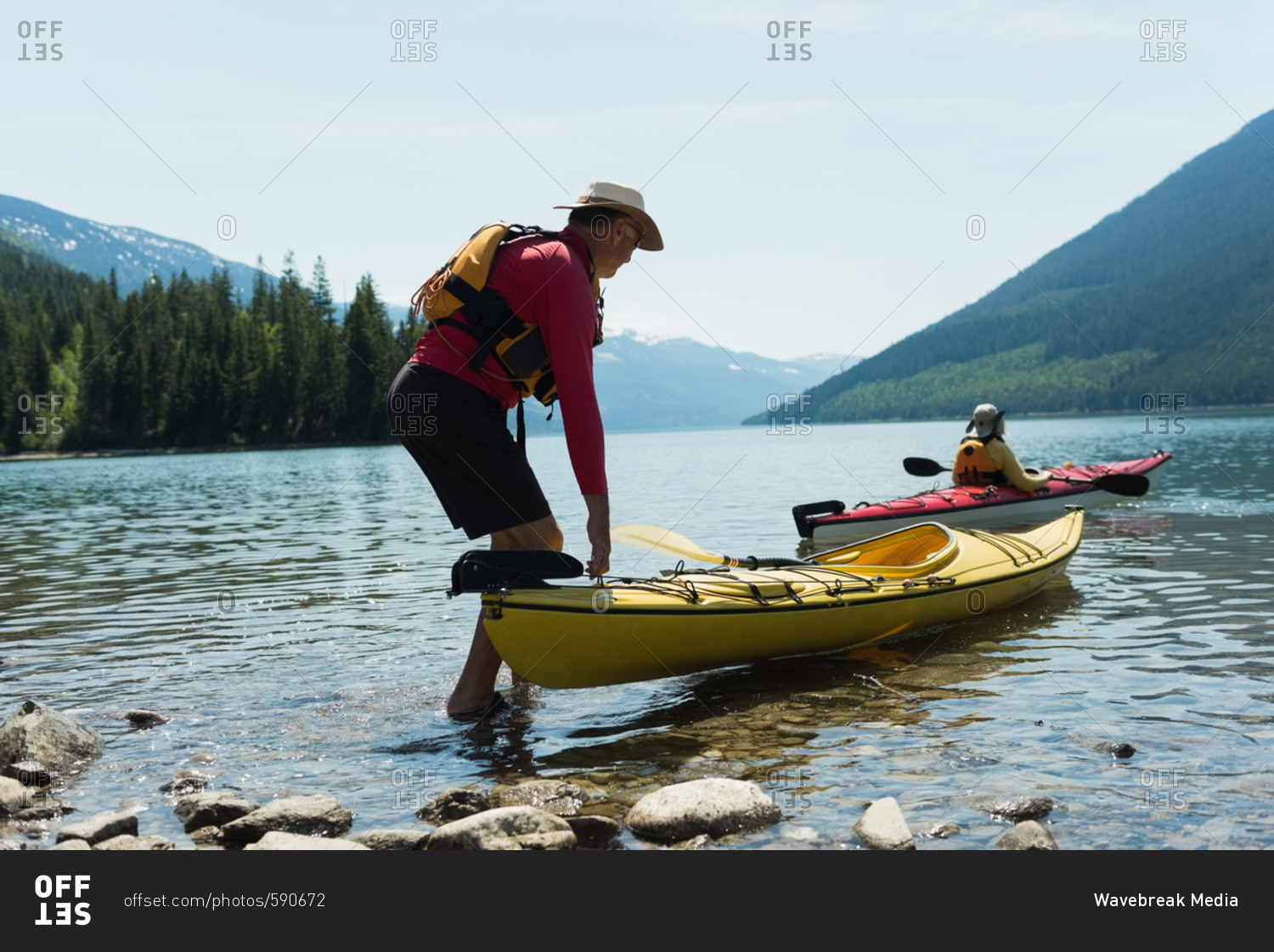 Man holding kayak while woman kayaking in lake against sky during sunny day