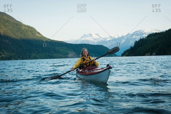 Happy woman oaring while kayaking in lake against sky